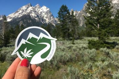 Person holding up a PotGuide sticker on their Colorado marijuana vacation 
