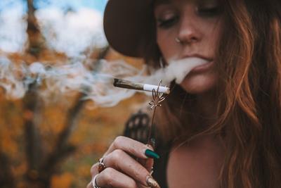Women with red hair smoking a joint, held by a gold roach clip, with smoke blowing around in the wind.