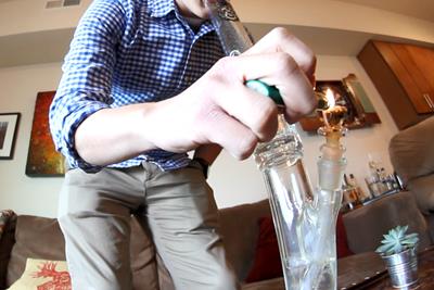 Man using a lighter to ignite weed and take a hit out of a glass marijuana bong