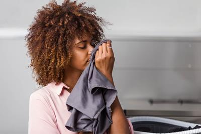 Black woman smelling a grey piece of clothing next to washing machine.