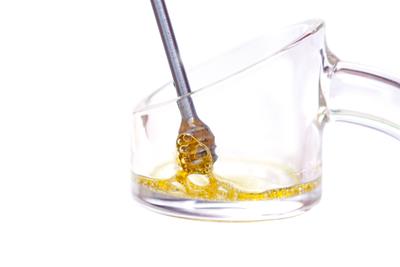 Dabber with golden concentrate being touched against a quartz banger.