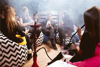 friends sitting in a circle, sitting on black and white chairs, smoking hookah in a smoke filled room 